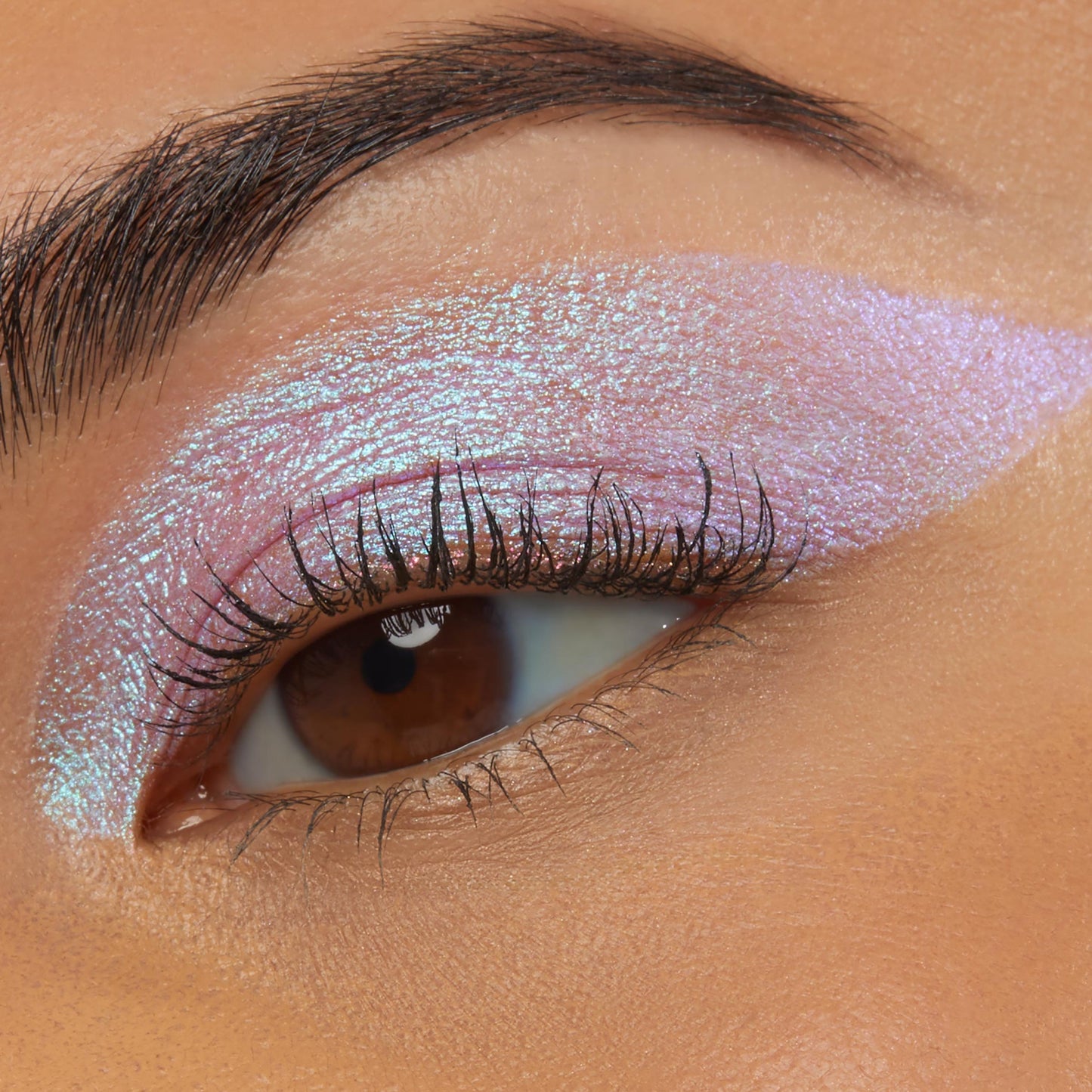 Close-up of an eye wearing Colourpop Disco Disco Shadow Stix, showing a bold wing of iridescent pink-lilac shimmer blended across the lid and crease against smooth warm-toned skin, highlighting the creamy metallic eyeshadow finish.